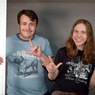 Młody mężczyzna i kobieta trzymają białą ramę jedną ręką, drugą pokazują znak ASL I love you