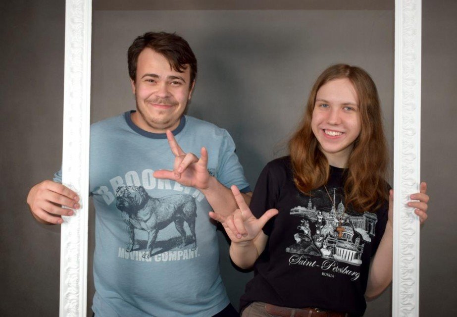 usłysz nas (11) Młody mężczyzna i kobieta trzymają białą ramę jedną ręką, drugą pokazują znak ASL I love you