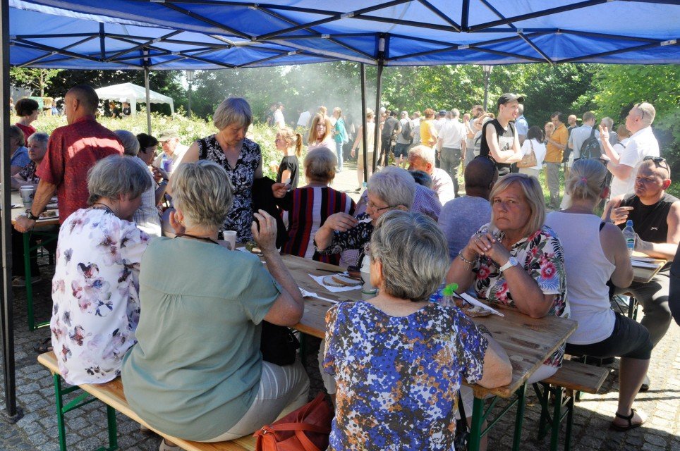 Grupa ludzi siedząca przy piknikowych stołach pod niebieskimi namiotami
