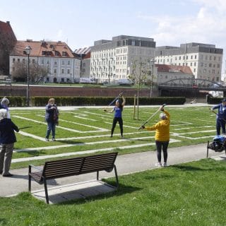 grupa seniorów wykonuje ćwiczenia z pomocą kijków na nabrzeżu Odry