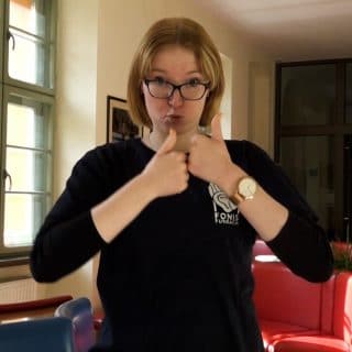 Kobieta pokazuje w języku migowym znak słowa "konkurs"