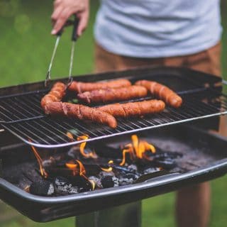 Osoba szczypcami przekłada kiełbasę na grillu