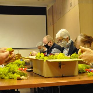 Seniorzy siedzą przy stole, na którym w kartonach jest mech chrobotek