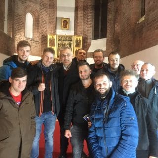 W kościele grupa mężczyzn ustawiona wokół Wojciecha Bartnika pozuje do zdjęcia