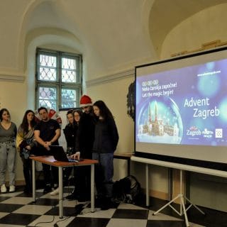 Grupa młodzieży z Chorwacji stoi w sali obok ekranu, na którym wyświetlona jest prezentacja o zwyczajach świątecznych
