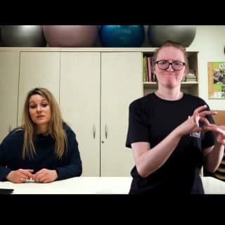 Kadr filmu. Przy stole siedzi pani psycholog, obok tłumacz języka migowego