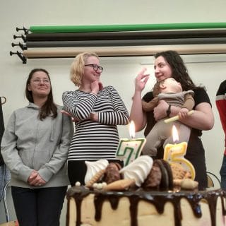 Tort z płonącymi świeczkami w kształcie liczby 75, a za nim trzy jubilatki