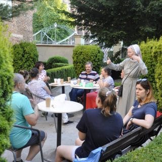 Kilka osób rozmawia siedząc w ogrodzie przy stolikach