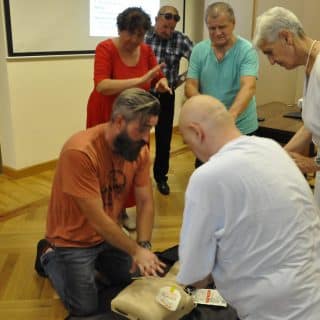 Instruktor i kursant pochylają się nad fantomem, stojący dokoła ludzie przyglądają się im