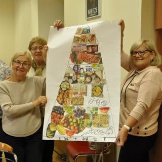 Trzy kobiety prezentują własnoręcznie wykonany plakat z piramidą zdrowego żywienia