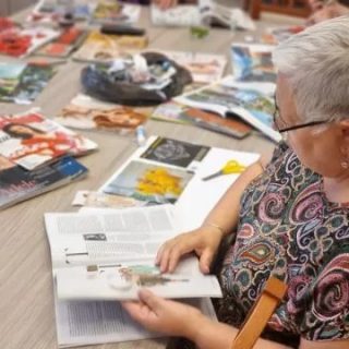 Kobieta z otwartą książką przy stole na którym leżą gazety i inne rzeczy