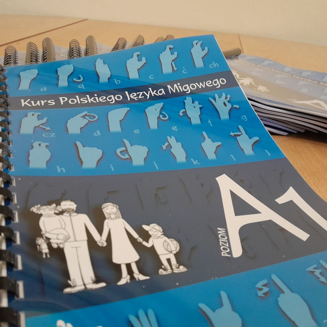 Niebieska okładka podręcznika, na niej na tle dłoni pokazujących litery rysunek rodziny i podpis poziom A1