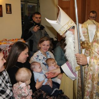 Święty Mikołaj pochyla się nad trójką niemowlaków trzymanych przez trzy kobiety