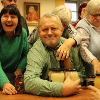 Mężczyzna trzyma kilka słoików z miodem, sięgają po nie stojący wokoło ludzie