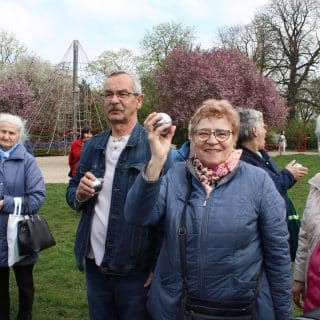 Grupa seniorów w parku, na pierwszym planie kobieta z podniesioną metalową kulą