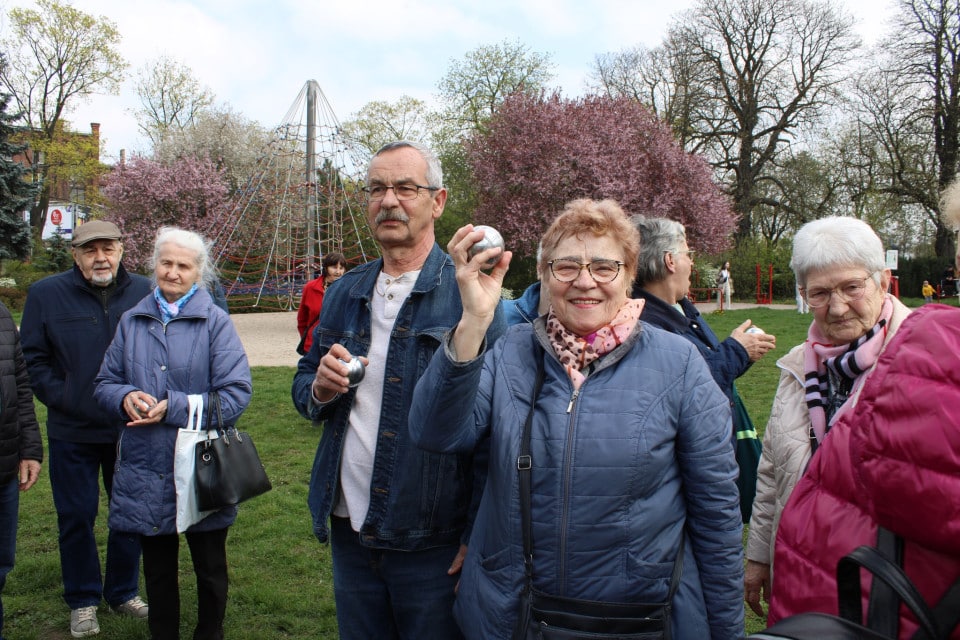Grupa seniorów w parku, na pierwszym planie kobieta z podniesioną metalową kulą