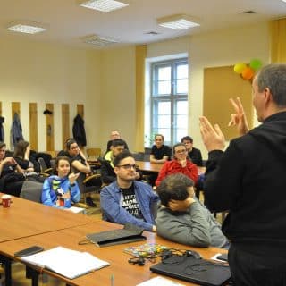 Kilkanaście osób w sali. Przed nimi stoi migający mężczyzna