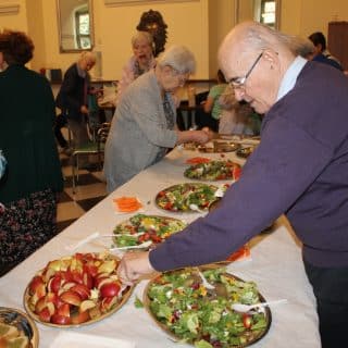 Seniorzy sięgają po zdrowe przekąski ustawione na stole