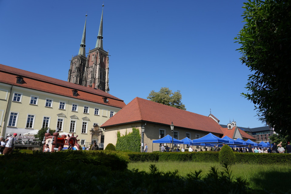 Plac festynowy z dmuchańcem i niebieskimi namiotami, w tle górują wieże katedry