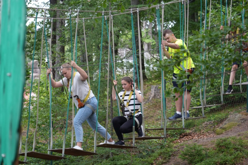 Kolonie w Karkonoszach2 Trzy osoby idą po deskach zawieszonych na sznurach w parku linowym