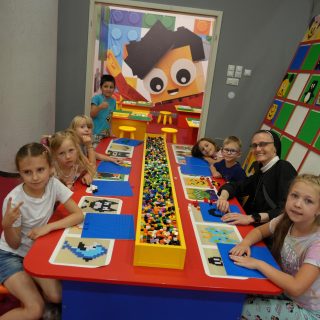 Grupa dzieci siedzi wokół stołu z klockami lego