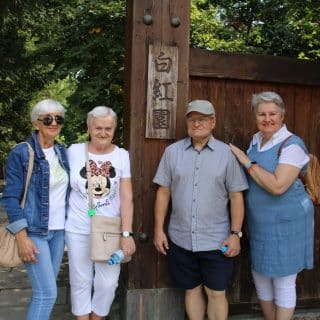 Czworo seniorów przy drewnianej bramie z japońskimi napisami