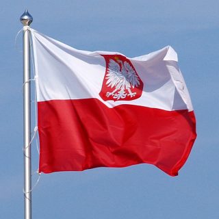Biało czerwona flaga z polskim godłem powiewa na maszcie