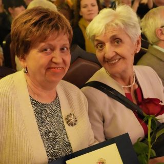 Dwie uśmiechnięte kobiety na tle sali wypełnionej ludźmi