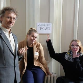 Trzy osoby przy wiszącej na ścianie kartce z napisem "Workshop Polen"