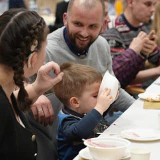 Dziecko pije z przechylonej miseczki, obok rodzice