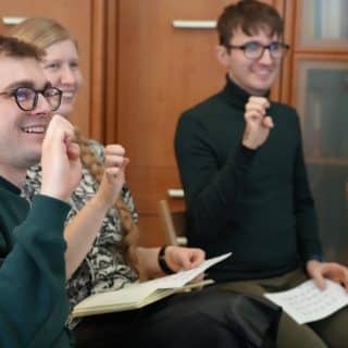 Trzy uśmiechnięte osoby pokazują znaki alfabetu migowego