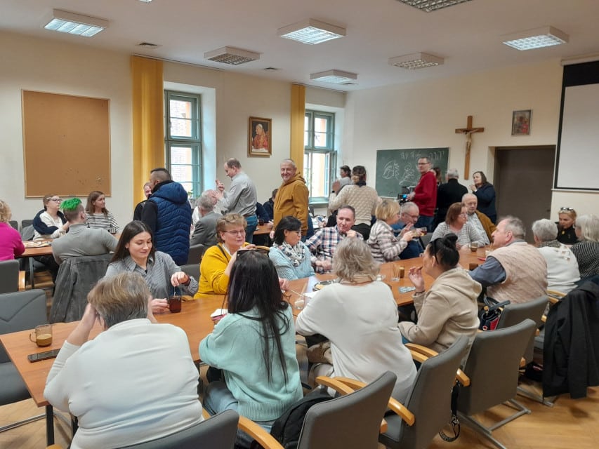 Spotkanie integracyjne w Fundacji FONIS Kilkadziesiąt osób w sali przy stolikach z kawą, herbatą i ciastkiem