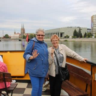Dwie seniorki na statku na tle rzeki i zabudowań miejskich na brzegu