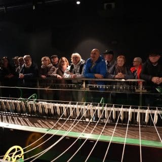 Grupa ludzi stoi wzdłuż dużej maszyny z nićmi