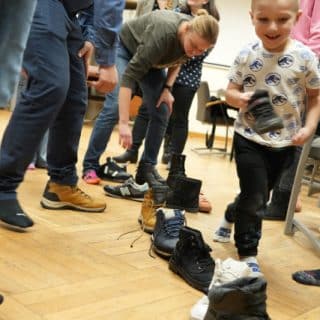 Kilka osób pochyla się przy butach ustawionych w rząd